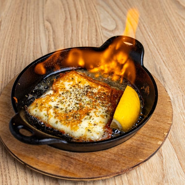 Saganaki, a flaming Greek cheese dish, served in a cast iron pan with a lemon wedge.