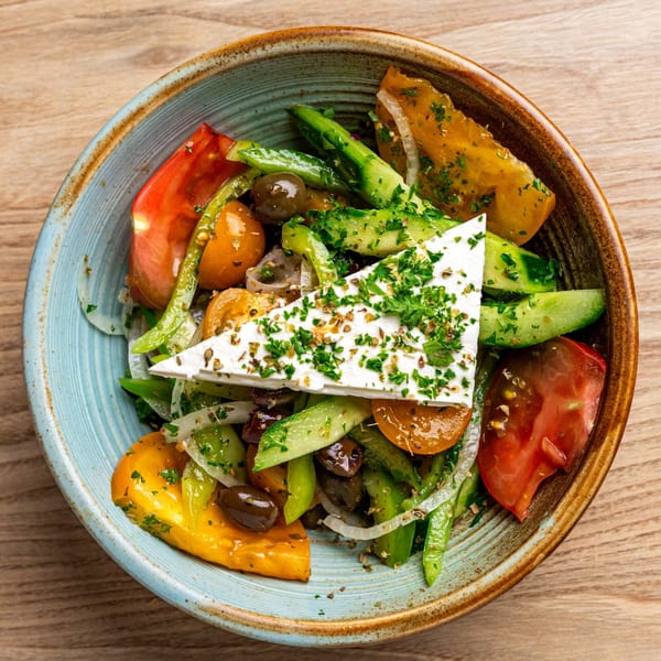 A vibrant Greek salad with feta, tomatoes, cucumbers, olives, and onions in a blue bowl.